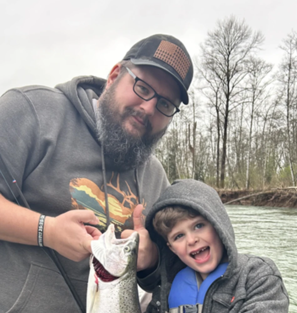 Jesse out on the river, holding up a fish he has just caught, with a delighted young helper beside him
